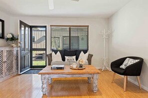 A room with a wooden coffee table, a black chair, a sofa with pillows, and a door leading outside.