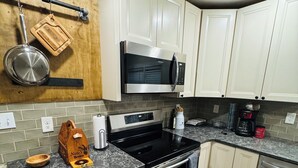 A kitchen with white cabinets, a stainless steel microwave, a black stove, and a wooden cutting board. - Cozy home in Milford/Harrington 
for relaxing stays! (Harrington)