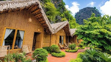 Una cabaña de madera con techo de paja, un porche con asientos y un jardín exuberante.