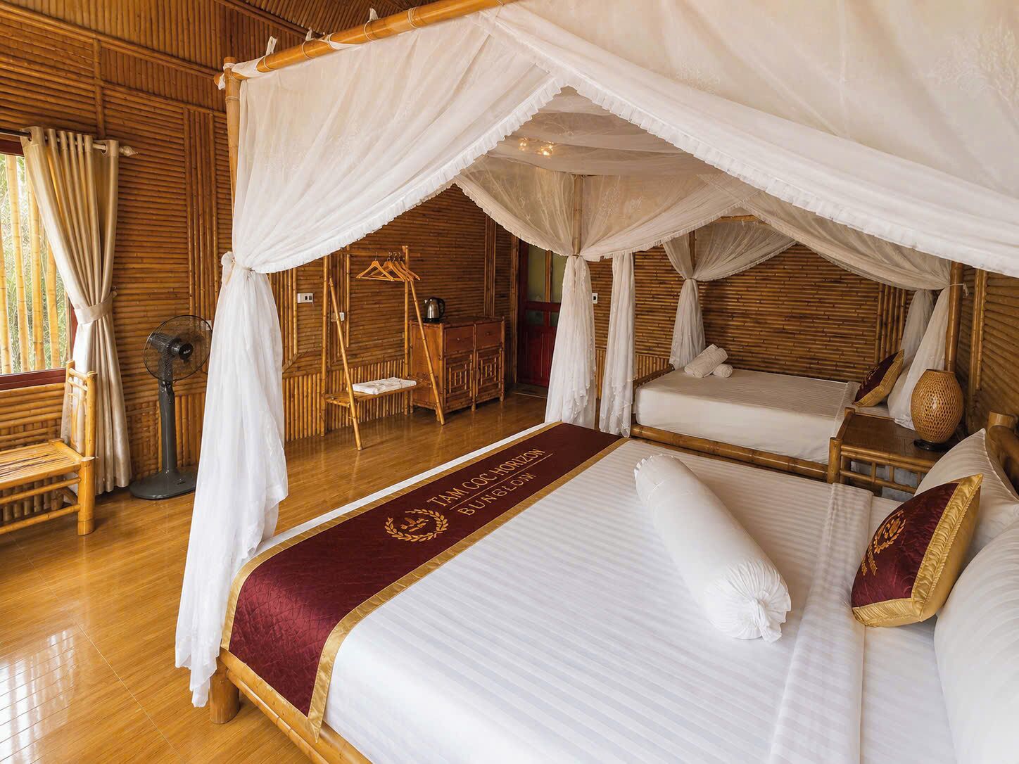 Un lit à baldaquin à quatre poteaux, agrémenté d’un couvre-lit rouge et doré, un plancher en bois et un mur en bambou.