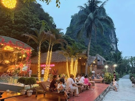 Un restaurante con terraza al aire libre, palmeras y montañas al fondo.