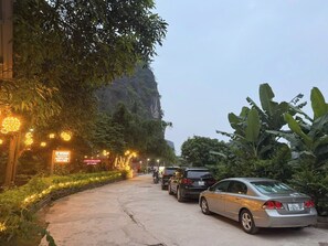 Un chemin pavé, bordé de lampadaires et de verdure, mène à un bâtiment sur lequel est apposée une enseigne.