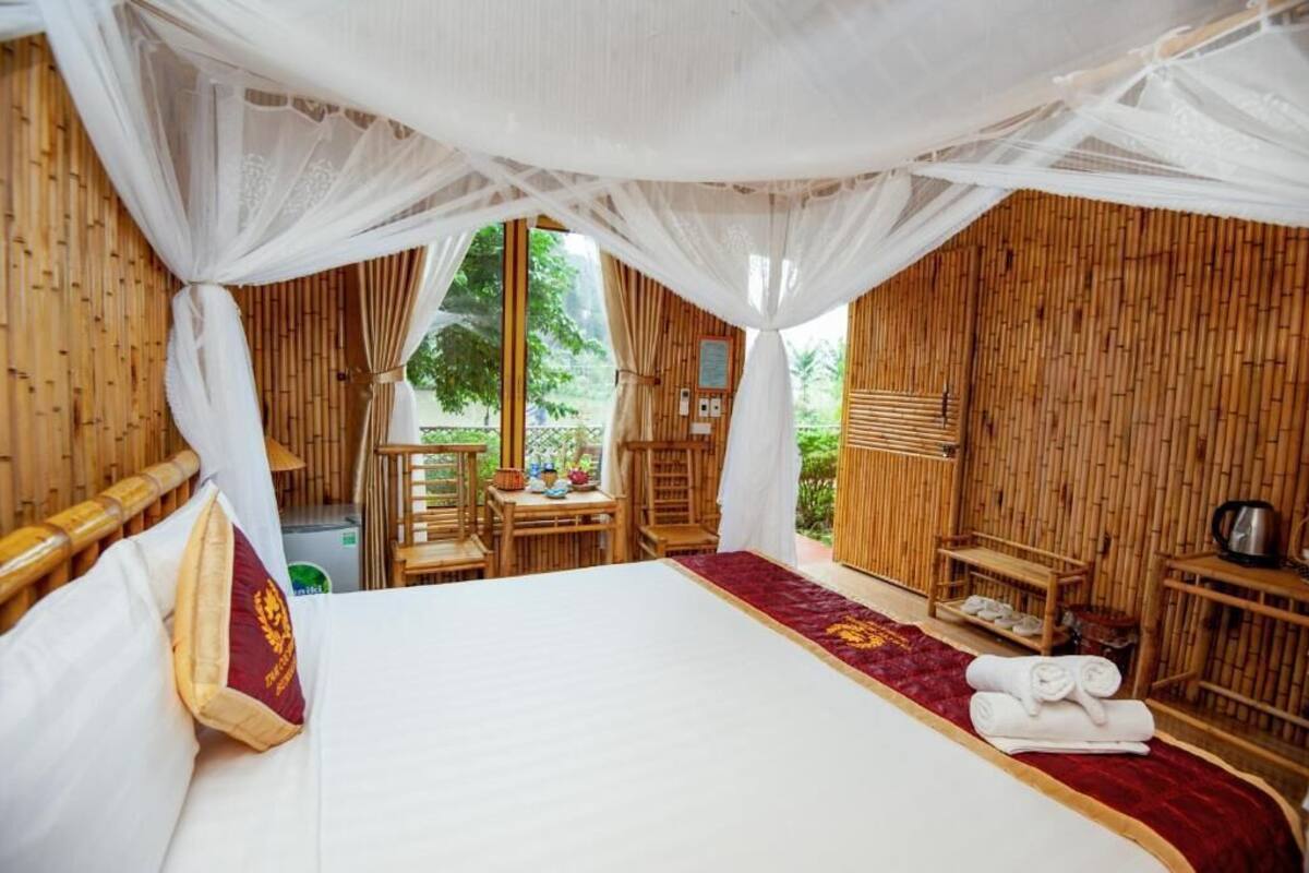 Una habitación con cama, una mesita, una silla y una ventana con vista a follaje.