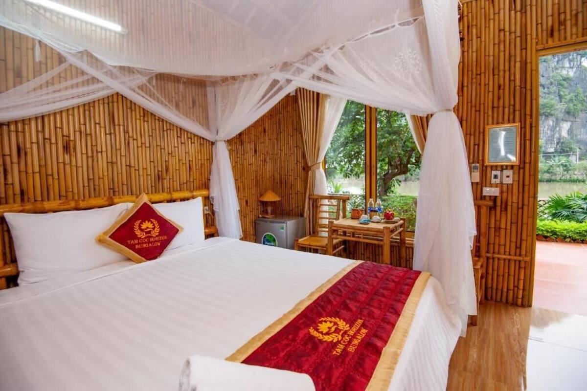 Una habitación con cama, una mesa con sillas, una lámpara y una ventana con vista a follaje.