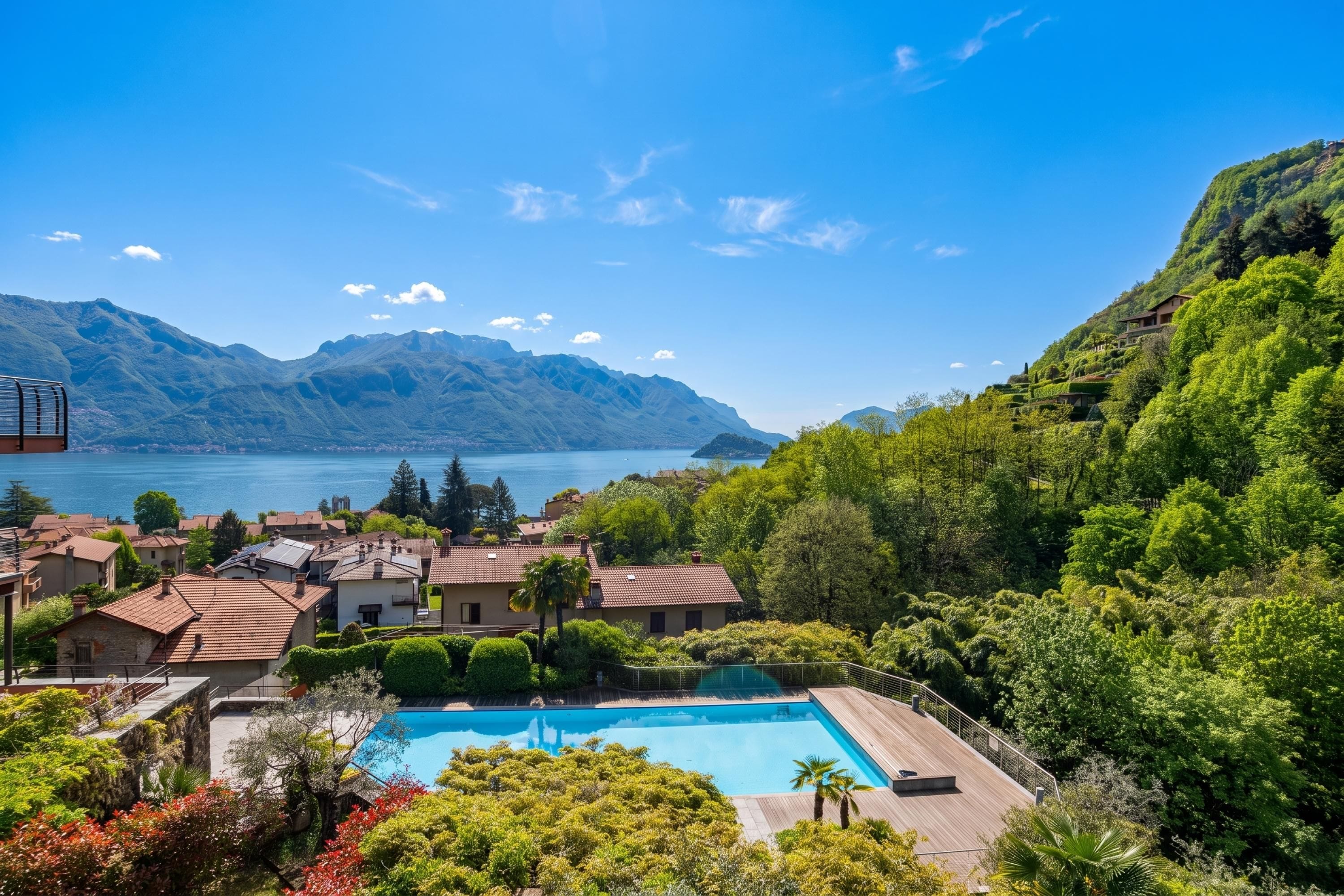 A residential area with a swimming pool, houses, and a lake with mountains in the background.