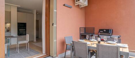 A dining area with a table set for two, a grill, and a sliding glass door leading to a kitchen.