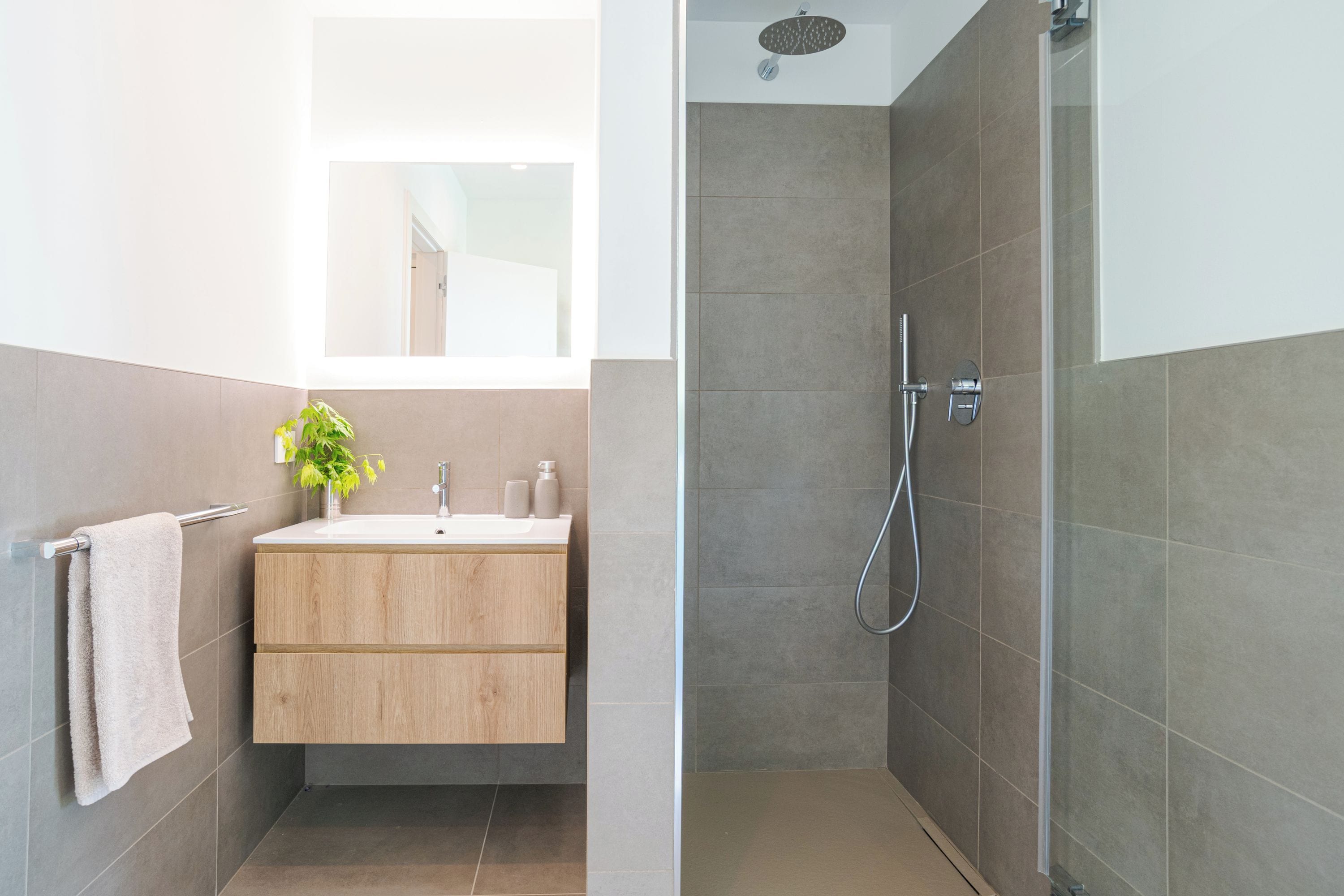 A modern bathroom with a wooden vanity, a towel rack, and a shower area with a glass door.