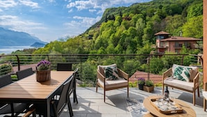 A terrace with a table, chairs, and a view of a mountainous landscape. - Magical Menaggio Vista (Menaggio)