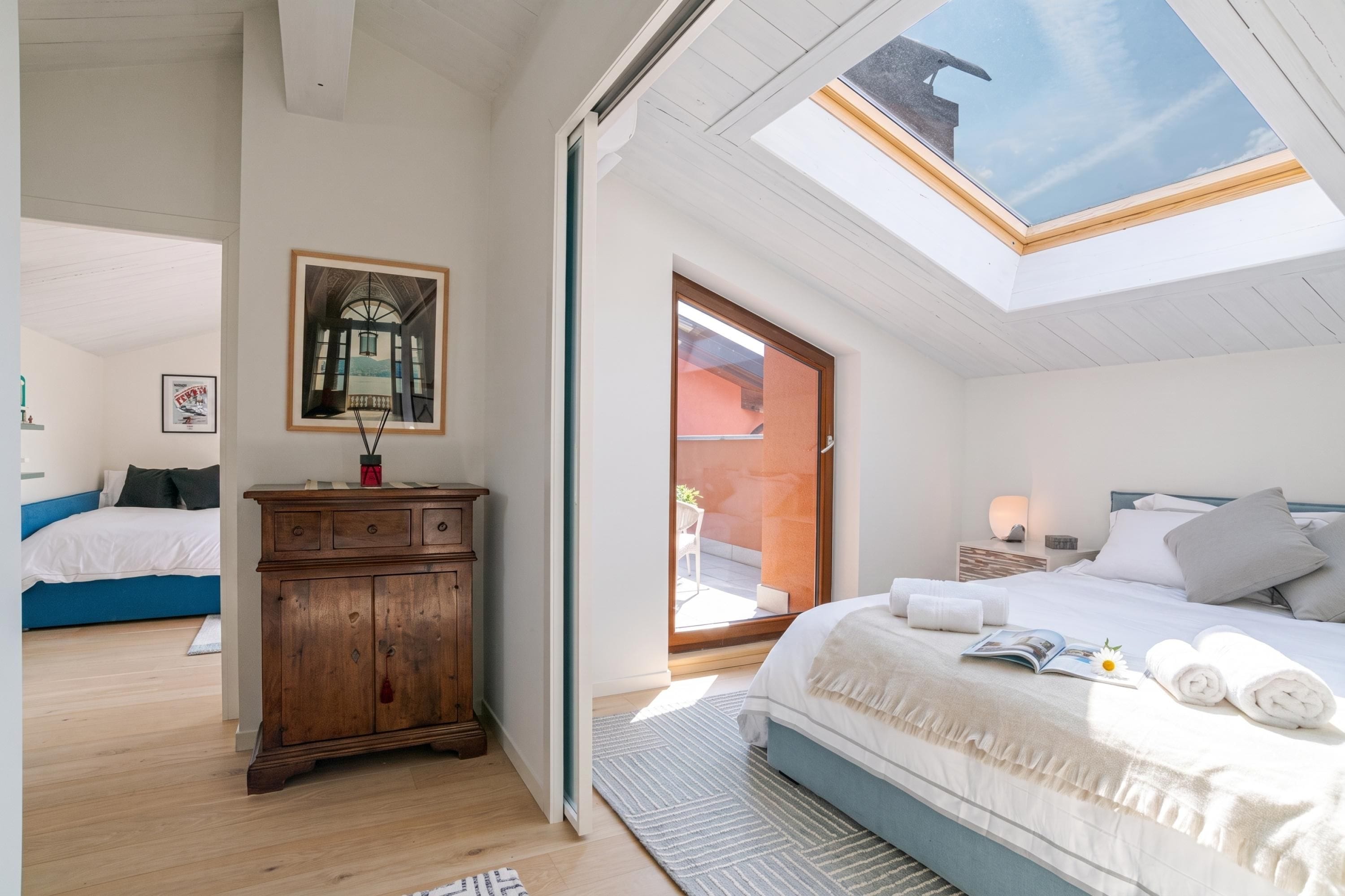 A bedroom with a skylight, a wooden dresser, a bed with towels, and a framed picture on the wall.