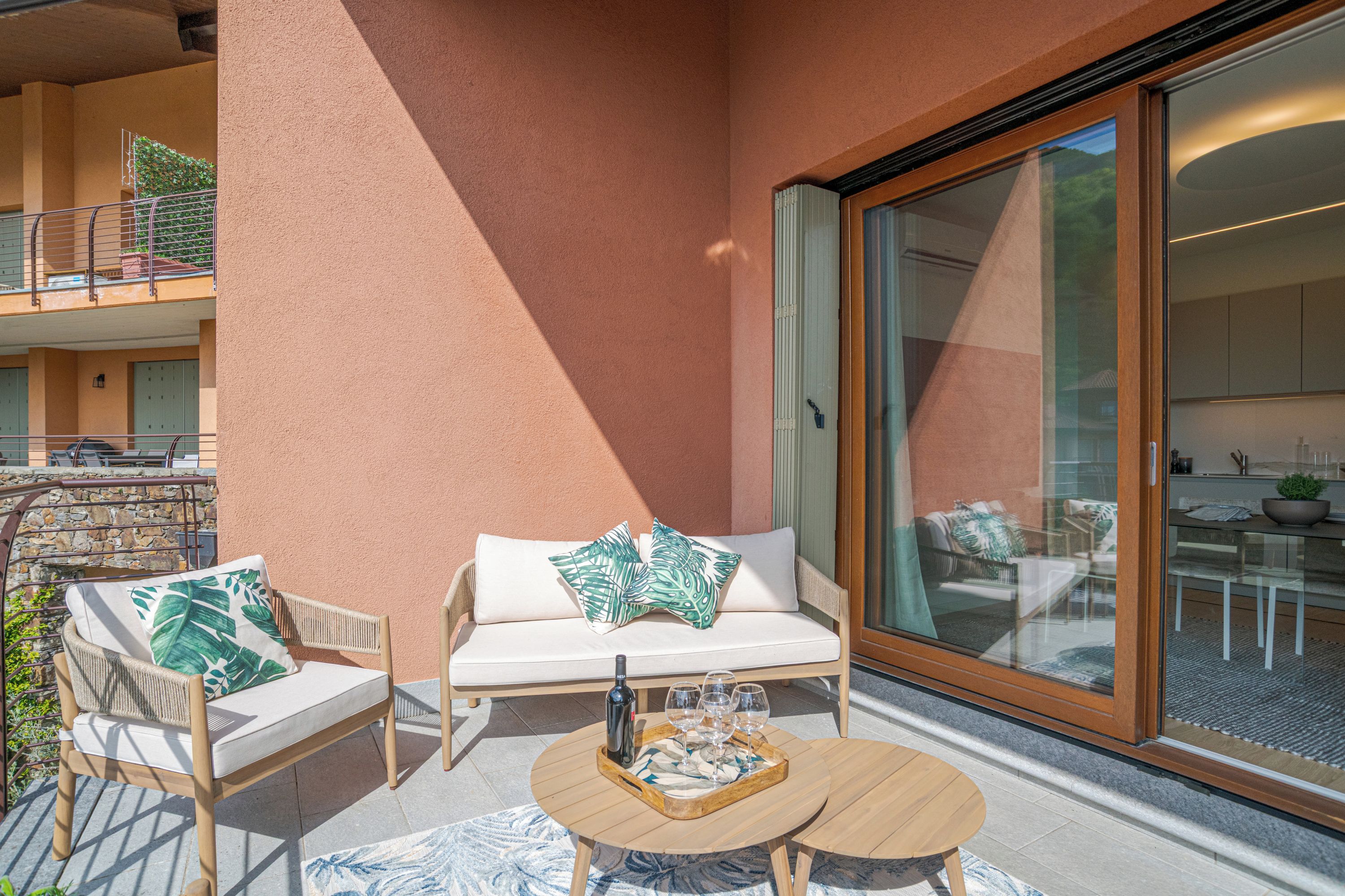A balcony with a sofa, chairs, a table, and a sliding glass door leading to an interior space.