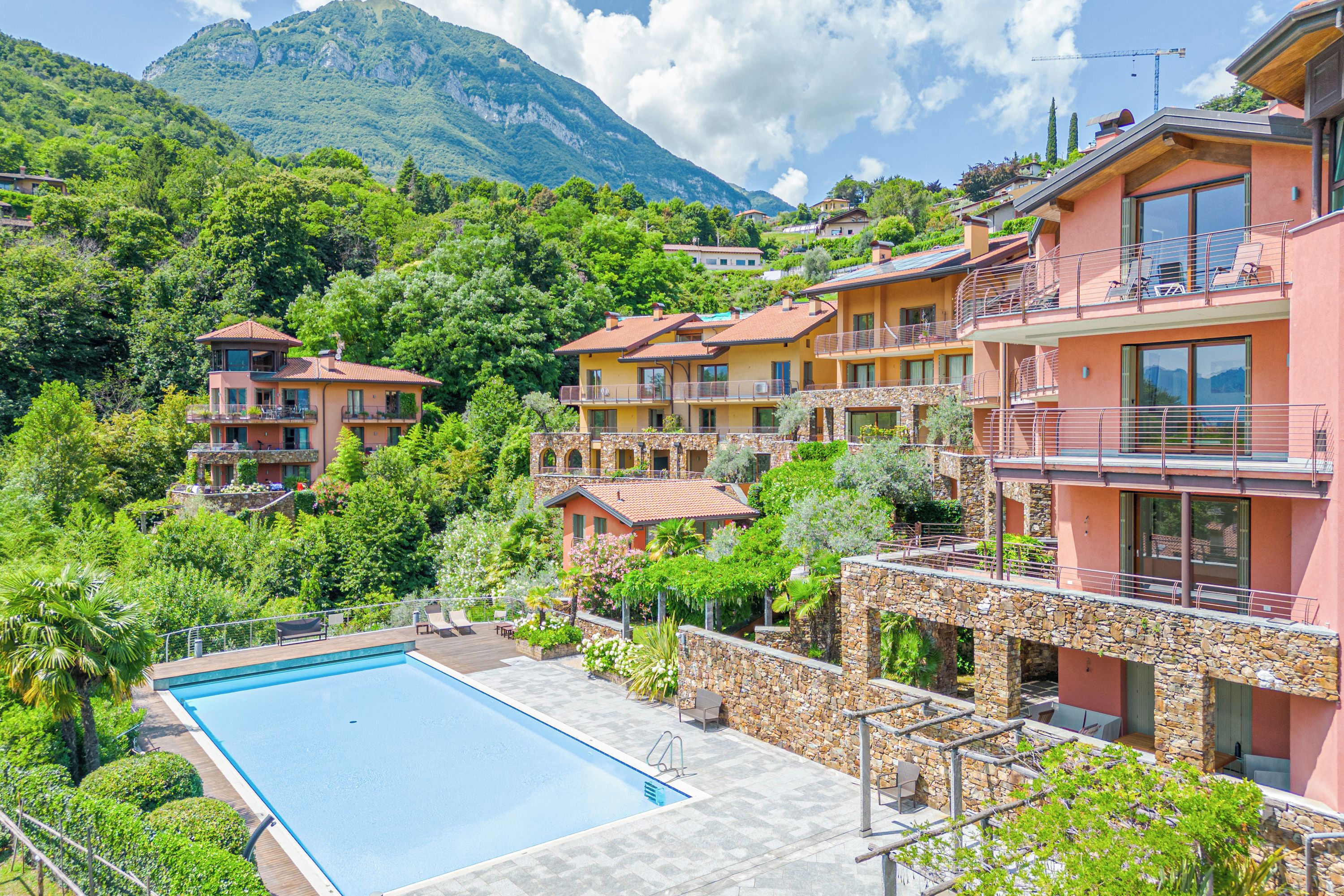 A multi-story hotel with a swimming pool, balconies, and a mountainous backdrop.