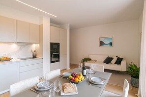 Cuina moderna amb armaris blancs, taula de dinar preparada per a quatre amb plats, gots i un plat de fruita.