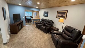 Ein Wohnzimmer mit Fernseher, Ledersofas, einem Essbereich und einer Küche im Hintergrund.