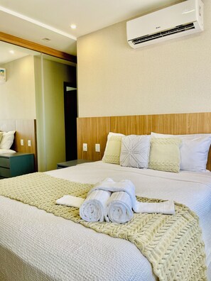 A hotel room with a bed, a wooden headboard, a wall-mounted air conditioner, and a bedside table. - 3-bedroom apartment with a suite, comfortable, quiet, and well located (Aracruz)