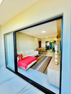 A modern living room with a sofa, a red blanket, a dining area with a table and chairs, and a kitchen in the background. - 3-bedroom apartment with a suite, comfortable, quiet, and well located (Aracruz)