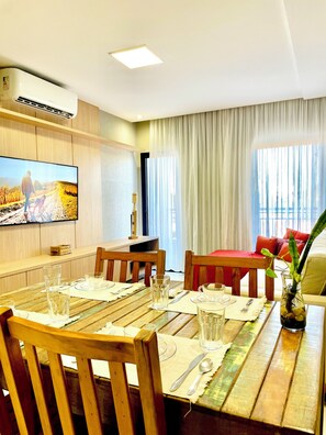 A dining area with wooden furniture, a television mounted on the wall, and a window with curtains. - 3-bedroom apartment with a suite, comfortable, quiet, and well located (Aracruz)