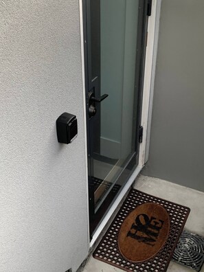 Una puerta con un panel de vidrio, un timbre negro y un felpudo marrón con un logo.