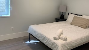 A bedroom with a bed, a nightstand, a lamp, and a window with blinds. - Room-brand new 2 Bedrooms (District of North Vancouver)