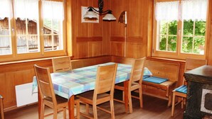 Une salle à manger en bois avec une table dressée pour quatre personnes, des chaises en bois et un banc.