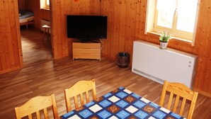 Une pièce en bois avec une télévision, un radiateur, une fenêtre, une table et, au fond, un lit superposé.