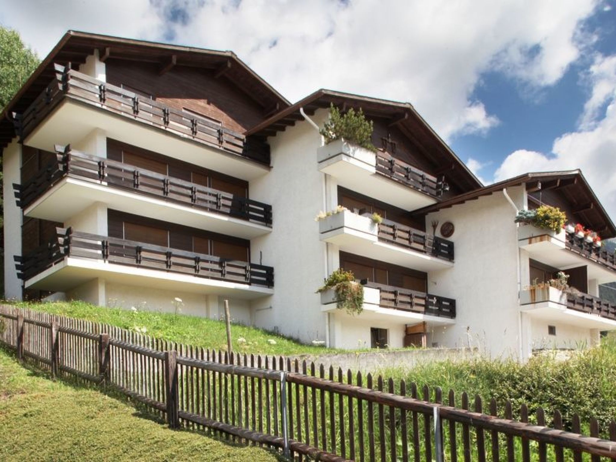 A multi-story hotel with balconies, a wooden fence, and a clear sky.