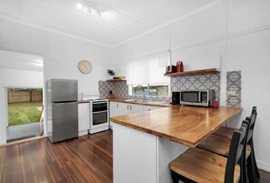 A modern kitchen with white cabinets, a wooden countertop, a stainless steel refrigerator, a microwave, and a clock on the wall.