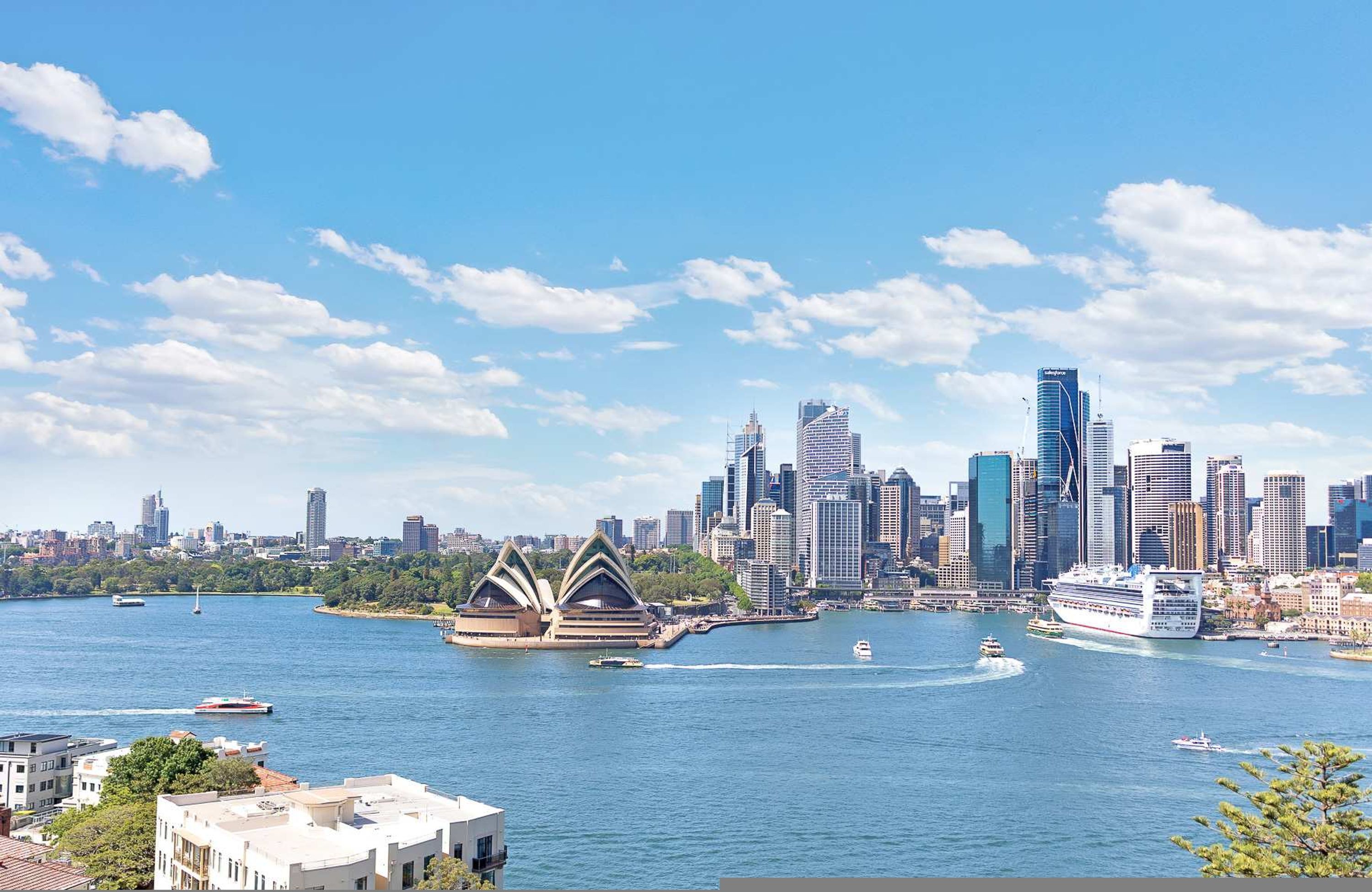Stadsbeeld met moderne gebouwen, een groot cruiseschip en het Sydney Opera House.