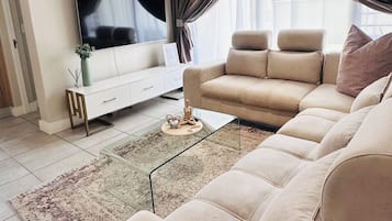 Un salon moderne avec un grand canapé, un téléviseur à écran plat, une table basse et un ventilateur de plafond.