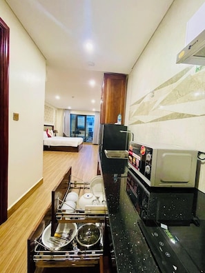 A compact hotel room with a kitchenette, a bed, a small dining area, and a view of the city. - Seven Sea Villa Hotel & Apartment (Da Nang)