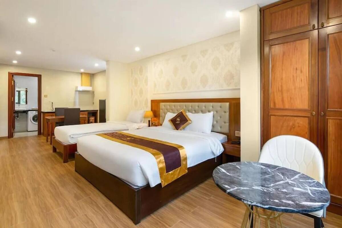 A hotel room with a large bed, a small table, a chair, a wardrobe, and a bathroom visible in the background.