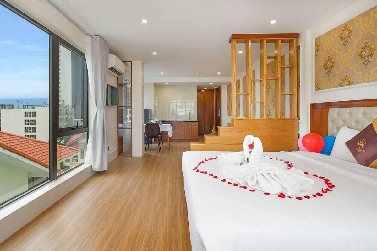 A hotel room with a large bed, a view of the city, a dining area, and a staircase.