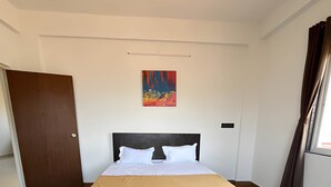 Een hotelkamer met een bed, houten vloer, een deur, een raam met gordijnen en een schilderij aan de muur.
