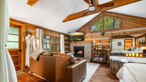 A log cabin interior with a fireplace, wooden ceiling beams, a sofa, and a bed. - New Cozy Spa Cabin! Hot Tub, Sauna, Jacuzzi! 20% Off-New Listing Promotion! (Sevierville)