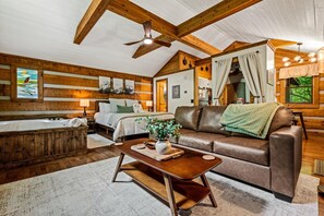 L’intérieur d’une cabane en rondins, avec un grand plafond en bois, un salon confortable doté d’un canapé en cuir, d’une table basse en bois, d’une cheminée et d’une grande fenêtre agrémentée de rideaux.