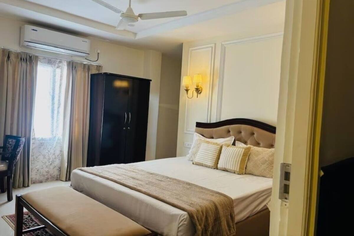 A hotel room with a bed, a desk, an air conditioning unit, and a ceiling fan.