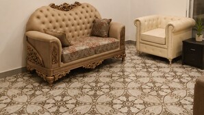 A room with a tufted sofa, a smaller armchair, patterned floor tiles, a ceiling fan, and a framed poster on the wall. - Hotel Granton By Carlton Suites (Hyderabad)
