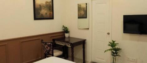 A hotel room with a bed, a desk, two wall-mounted lamps, a television, and a potted plant.