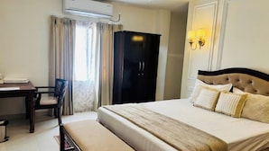 A hotel room with a bed, a desk, a chair, an air conditioning unit, and a wardrobe. - Hotel Granton By Carlton Suites (Hyderabad)
