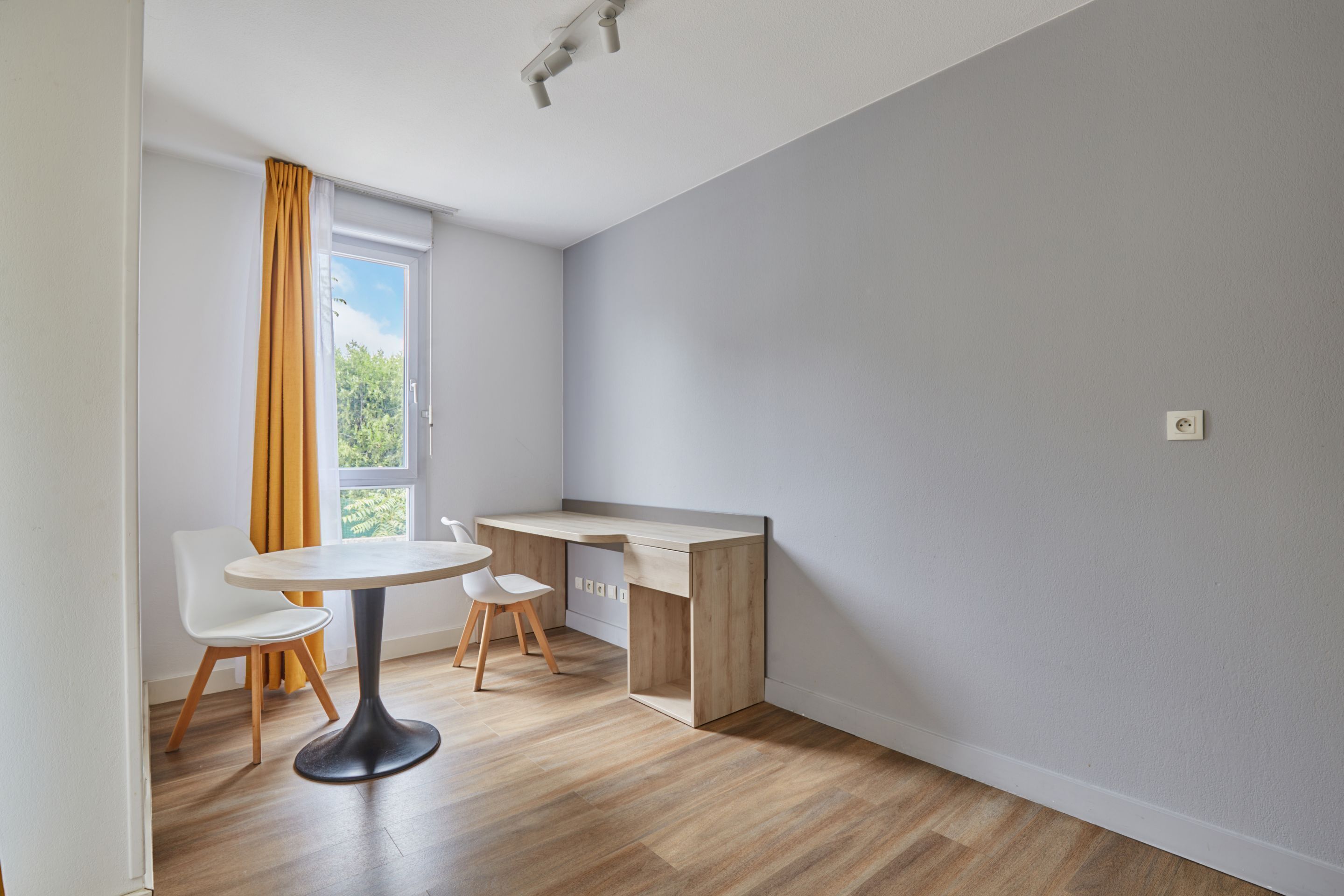 Une pièce moderne avec un bureau en bois, une chaise blanche et une petite table ronde.