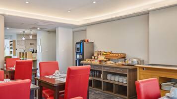 Un espace repas moderne avec des chaises rouges, un buffet proposant des plats et des boissons, et un téléviseur.
