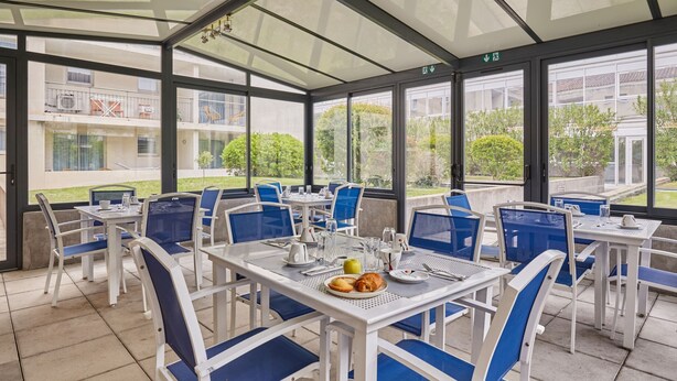A covered outdoor dining area with tables and chairs, a view of the building in the background, and a sign indicating an exit. - Studio Rénové + Climatisé | Wi-Fi Gratuit ! (Aix en Provence)
