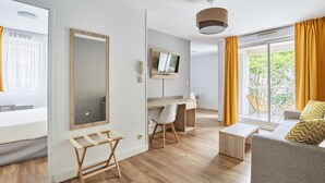 Una camera d'albergo moderna con pavimento in legno, un letto, una scrivania con sedia, una televisione e un divano con cuscini.