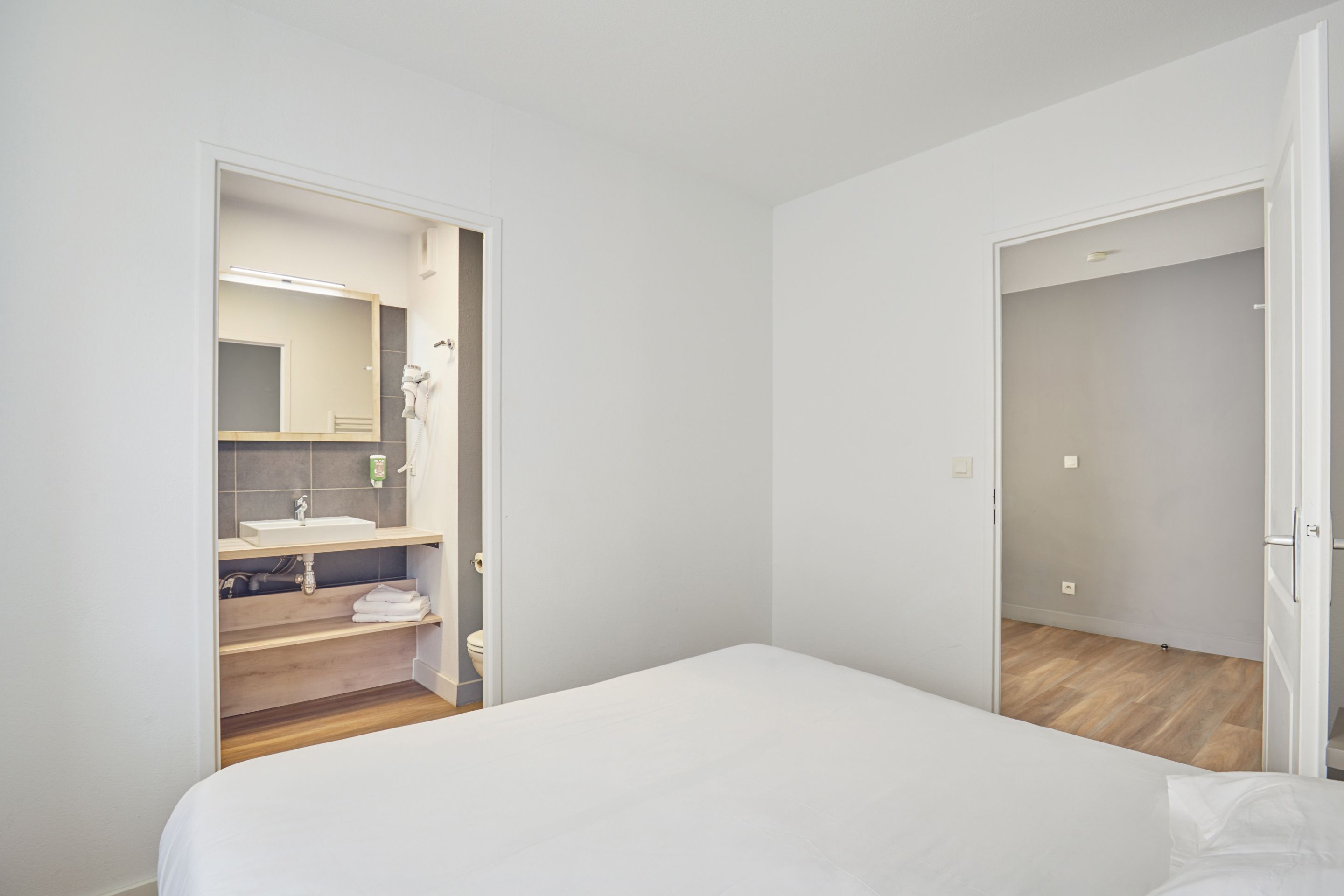 Un dormitorio minimalista con cama, un baño con espejo y una puerta que conduce a otra habitación.