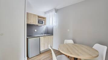 Una cocina compacta con microondas, pileta y heladera pequeña. Hay una mesa redonda de madera con dos sillas blancas.