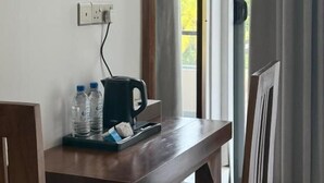 A room with a wooden desk, a power outlet, a kettle, and a window with curtains.