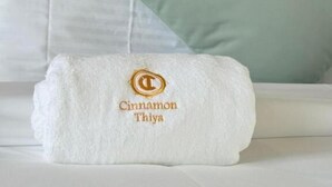 A neatly made bed with a folded white towel featuring a logo and text, a light green pillow, and a wooden headboard.
