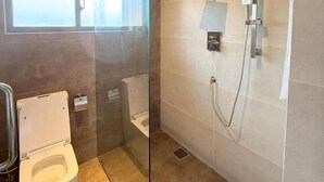 A modern bathroom with a glass shower enclosure, a toilet, and a large window providing natural light.