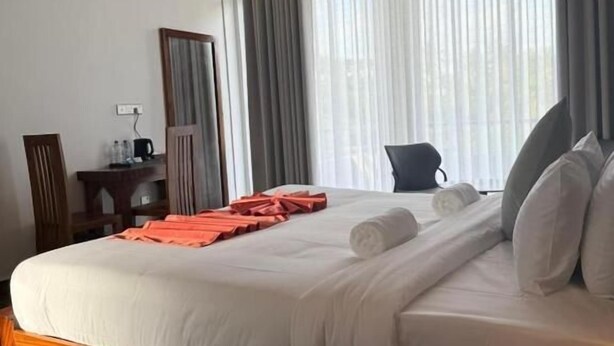 A hotel room with a bed, a desk, a chair, a mirror, and a window with curtains.