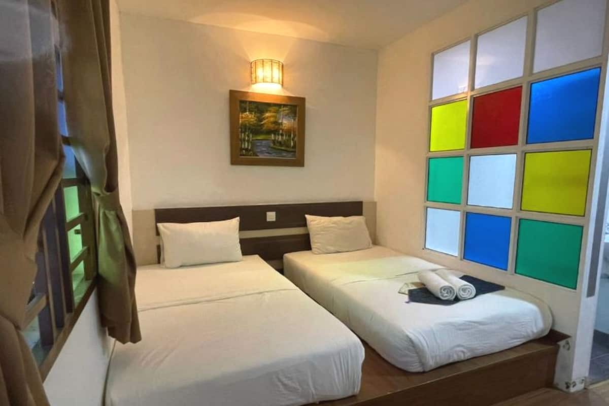 A hotel room with two beds, a painting on the wall, and a window with colorful panels.