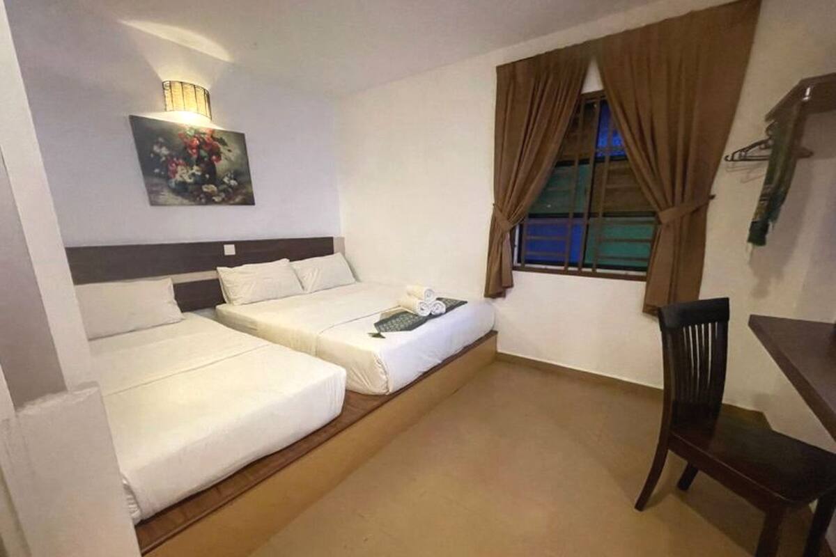 A hotel room with two beds, a desk, a chair, a painting, and a window with curtains.
